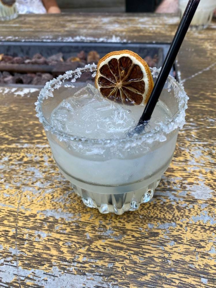 A mezcal cocktail with ice on a wooden table at Idle Hands in Austin, garnished with dried citrus and a salt rim. 